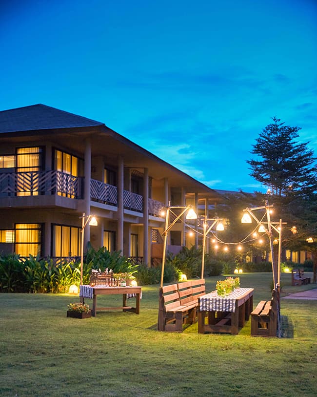 An evening view of the Wishing Tree Resort with benches and festive lights.